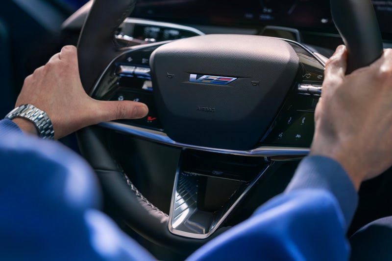 Close-up of a Man About to Press the V-Button on the 2026 OPTIQ-V Steering Wheel | Cadillac of Mahwah in MAHWAH NJ
